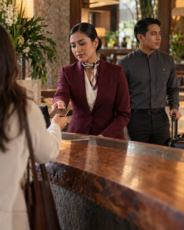 Uniformes para hotelería: recepcionista con blazer vino y botones con camisa de cuello mao en el lobby